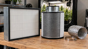 Particle and carbon filters with cannabis plants in a grow tent behind them